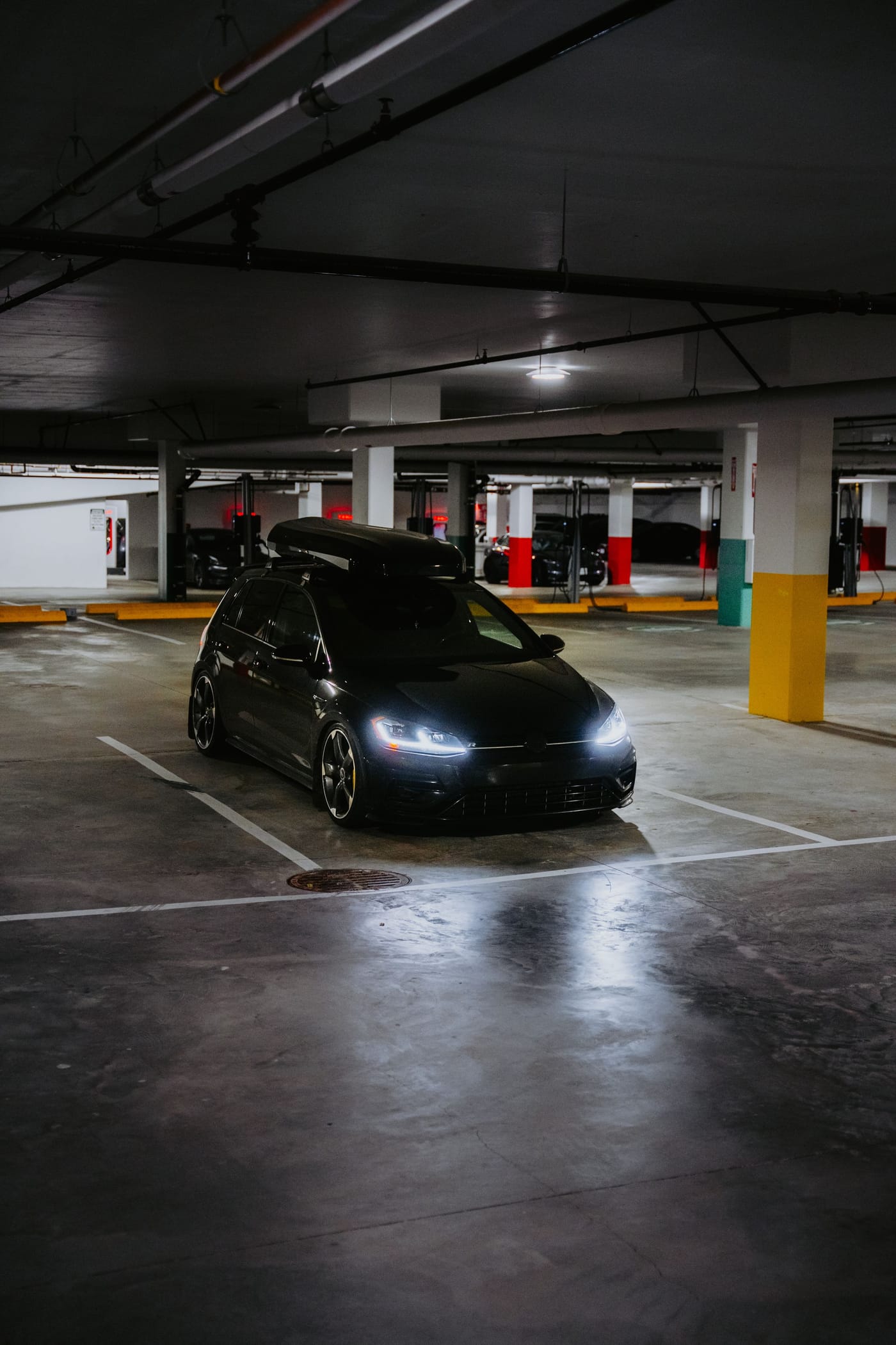 Schwarzer Personenwagen mit eingeschalteten Scheinwerfern in einer dunklen Garage.