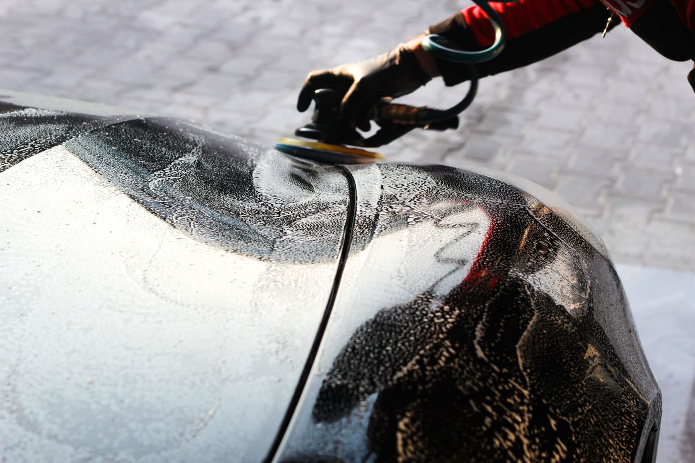 Pad auf einer nassen dunklen Motorhaube, nur die Hand sichtbar.